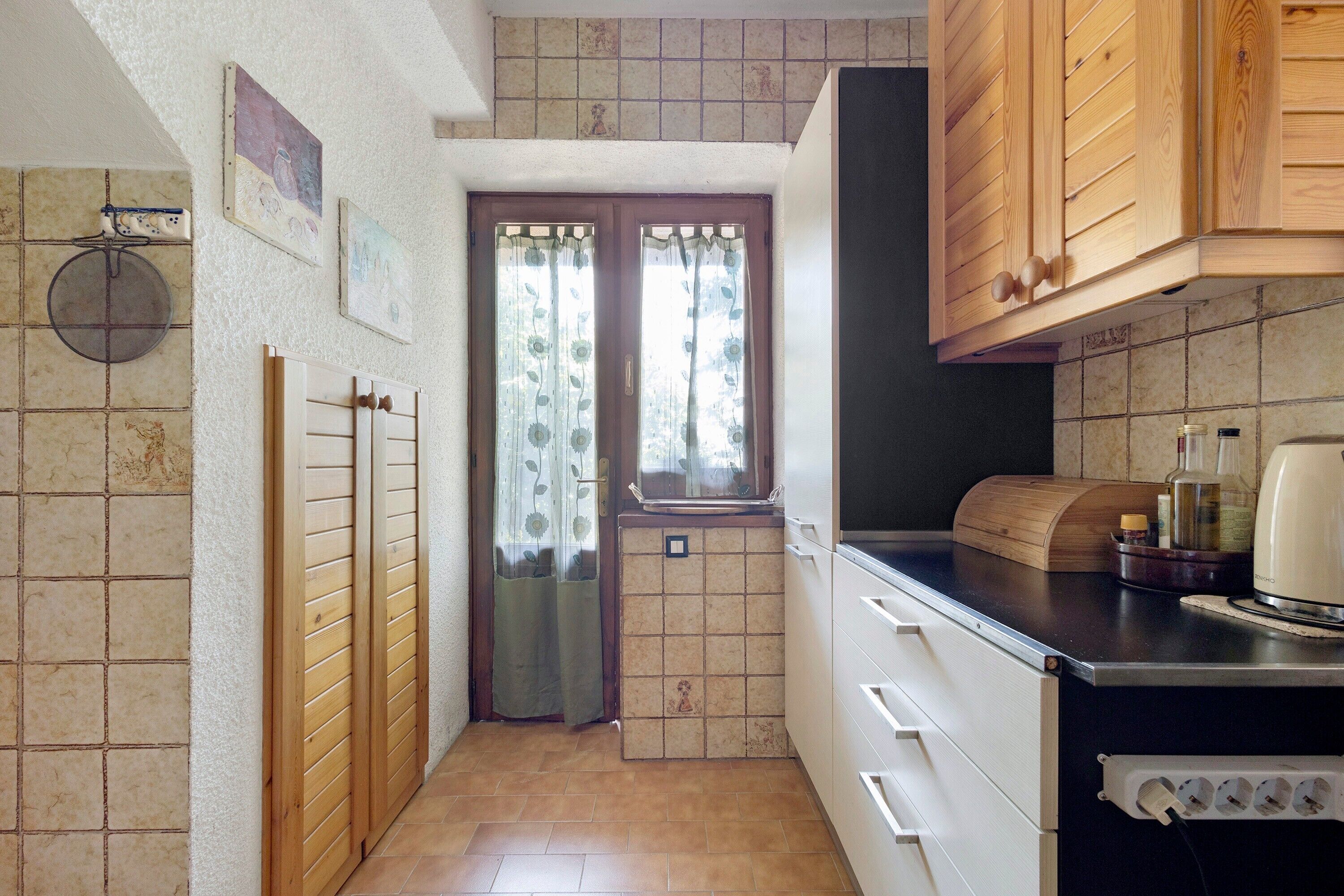 Una cucina compatta con mobili in legno, forno a incasso e una finestra con tende floreali.