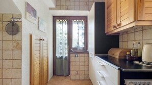 Eine kleine Küche mit Holzschränken, einem Einbauofen und einem Fenster mit blumigen Vorhängen.