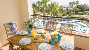 A wooden table set for breakfast with plates, cutlery, and a fruit basket, overlooking a pool and palm trees. - Spacious Family Stay Near the Beach (Linguizzetta)