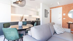 En moderne stue med sofa, spisebord, stole og et køkken med hårde hvidevarer.