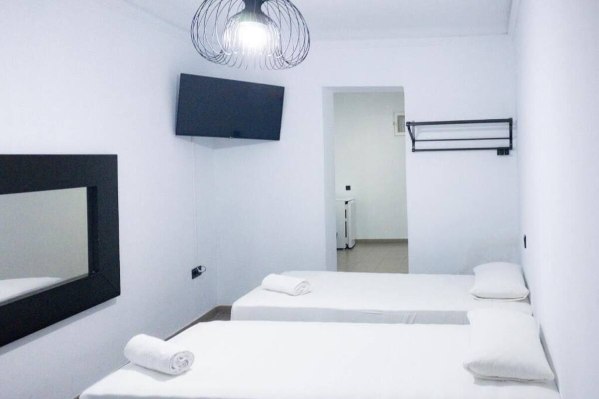 A hotel room with two beds, a large mirror, a flat-screen TV, and a modern light fixture.