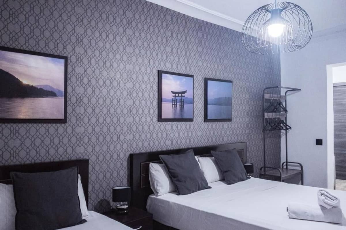 A hotel room with two beds, a patterned wall, framed pictures, a modern light fixture, and a view of the outdoors.