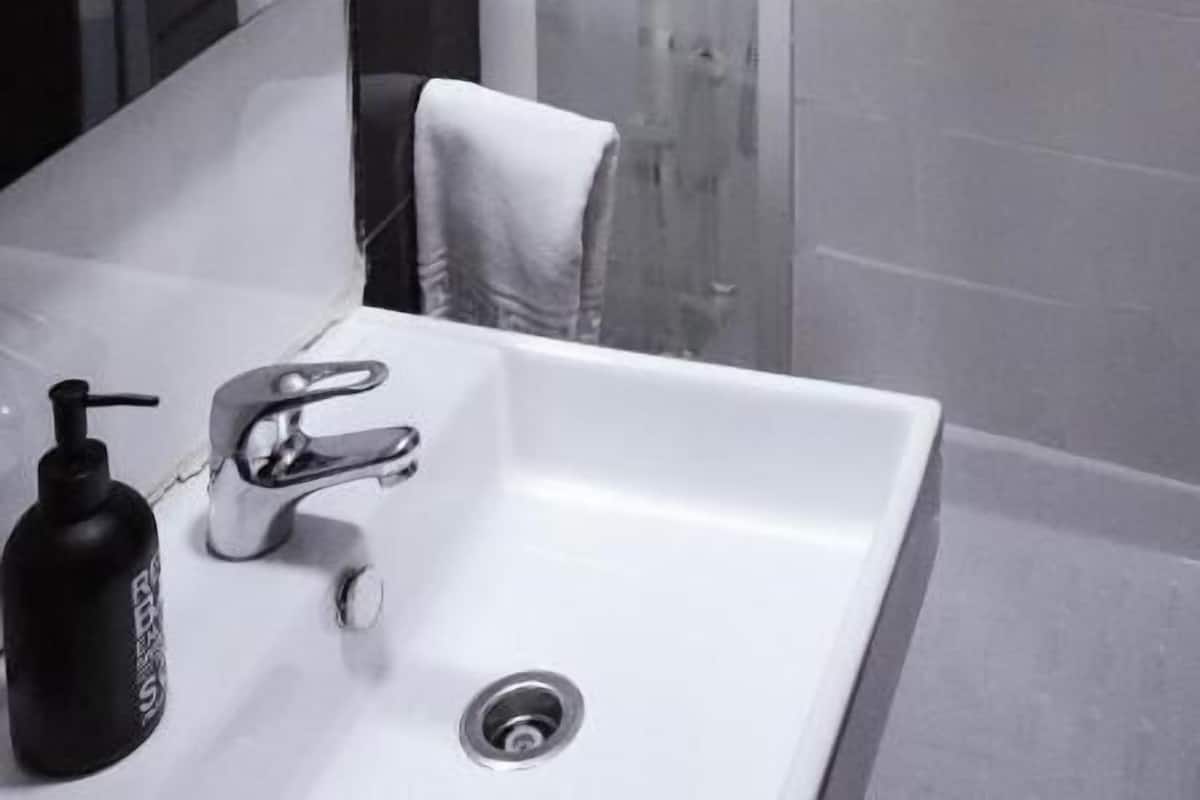 A bathroom with a white sink, a mirror, a shower enclosure, and a towel hanging on the wall.