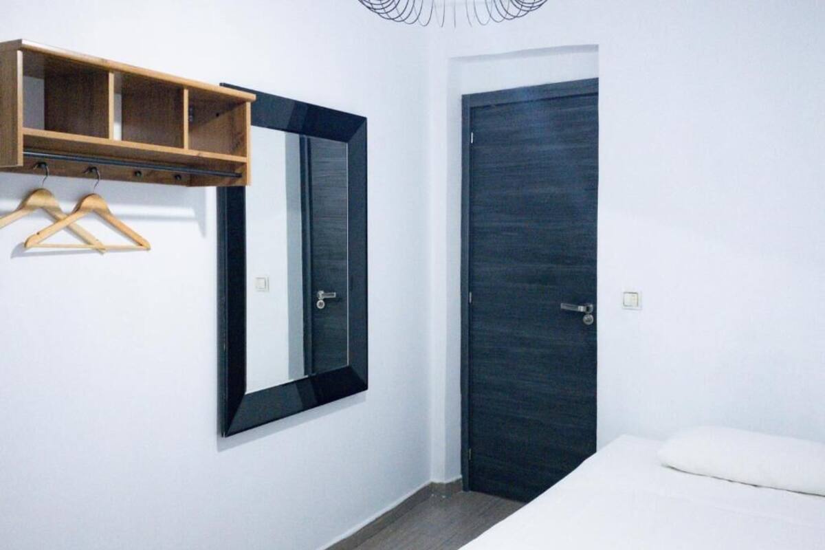 A bedroom with a dark door, a wooden shelf with hangers, and a mirror.