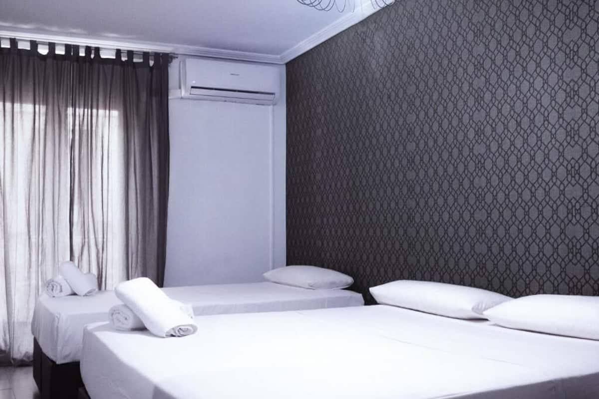 A hotel room with two beds, a window with curtains, an air conditioning unit, and a patterned wall.