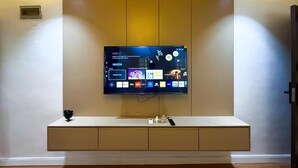 A modern hotel lobby with a large flat-screen TV mounted on a wall, a minimalist console table, and recessed ceiling lighting. - Wealth's Khort Apartment (Keffi)
