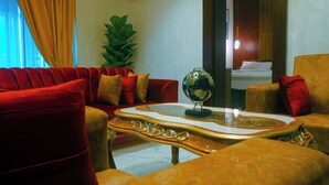 A living room with a red sofa, a matching armchair, a glass coffee table with a globe, and a potted plant. - Wealth's Khort Apartment (Keffi)
