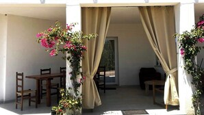 Un edificio de dos pisos con un balcón, un patio cubierto con cortinas y una mesa de comedor con sillas.