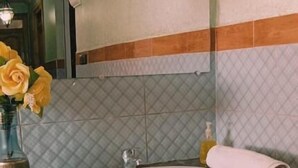 A bathroom with a marble sink, a mirror, a towel, a trash bin, and a vase with yellow flowers.