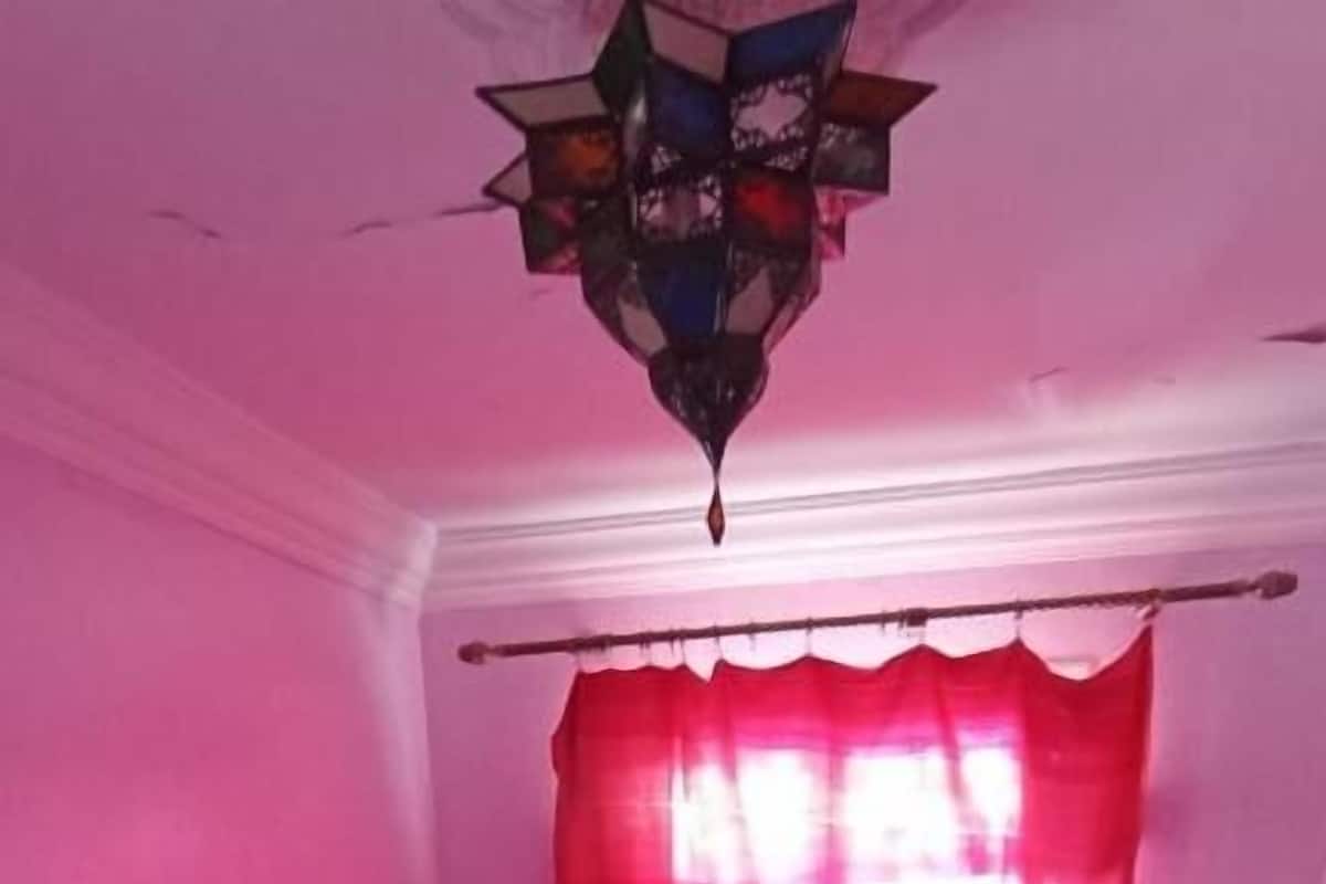 Un dormitorio con cama, mesita de noche, cortina roja y un elemento decorativo en el techo.