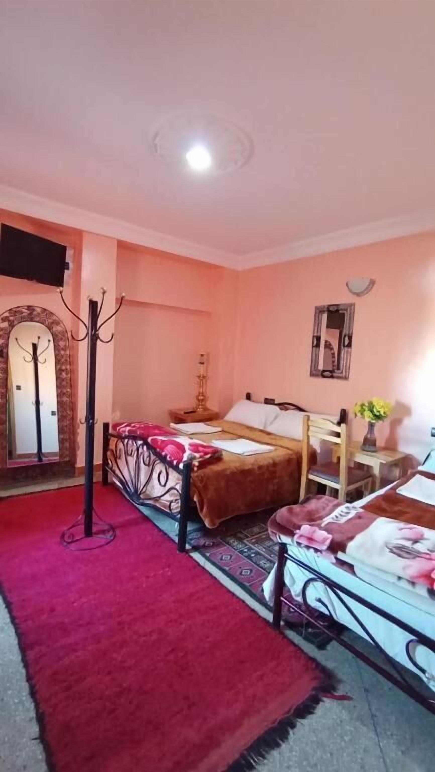 A bedroom with two beds, a red carpet, a coat rack, and a mirror on the wall.
