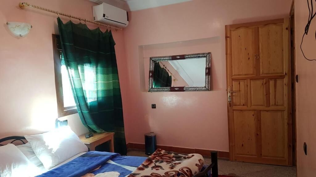 Un dormitorio con cama, ventana con cortinas, espejo, puerta de madera y unidad de aire acondicionado.