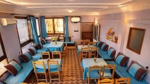 A hotel room with a checkered floor, multiple seating areas with tables and chairs, and a large window with curtains.