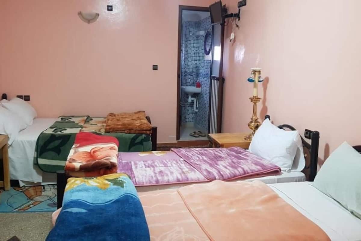 Una habitación con dos camas, un escritorio, una silla, una lámpara y un baño visible a través de una puerta abierta.