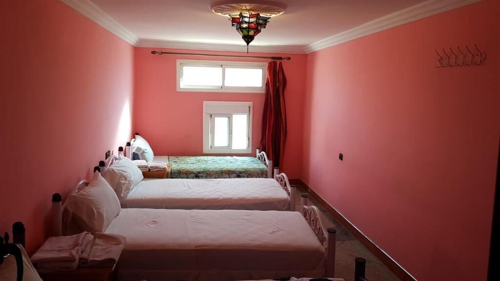Une chambre avec deux lits, une fenêtre, un lustre et un rideau rouge.