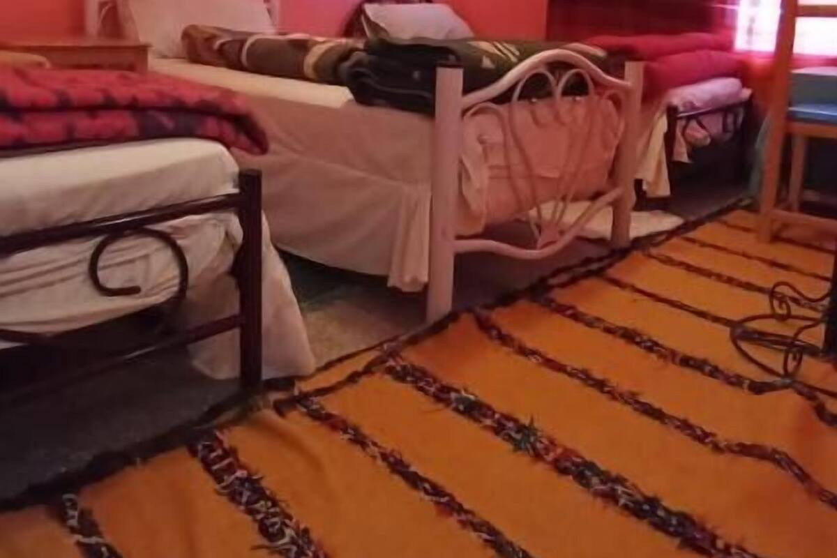 Una habitación con dos camas, una pared roja, un tapete estampado y una lámpara en el techo.