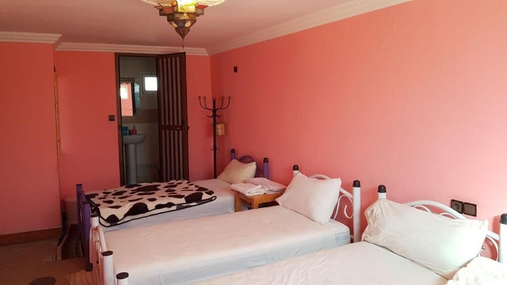 Een kamer met twee bedden, een plafondventilator, een kapstok en een zichtbare badkamer door een deur.