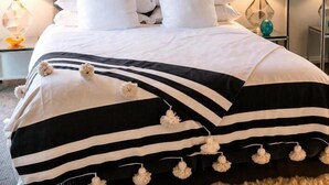 A bed with a tufted headboard, white bedding, and striped throw pillows with pom-poms.