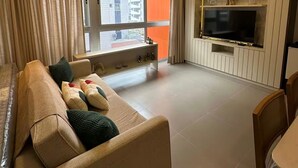 Moderni olohuone, jossa on sohva, televisio ja parveke, jolta avautuu näkymä kaupunkiin.