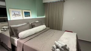 Moderni hotellihuone, jossa on suuri sänky, taulutelevisio ja kaksi kehystettyä kuvaa seinällä.