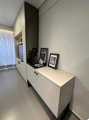 Ein modernes Wohnzimmer mit einer weißen Unterhaltungsanlage, einem großen Fenster mit leichtem Vorhang und einem gefliesten Boden.
