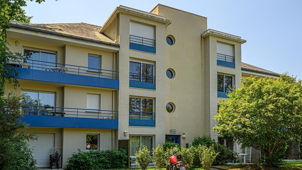 A multi-story residential building with balconies, a motorcycle parked in front, and a clear sky. - Comfortable House Stay for 6 in Plescop (Plescop)