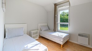 A bedroom with two beds, a window, a bedside table, and a radiator. - Comfortable House Stay for 6 in Plescop (Plescop)