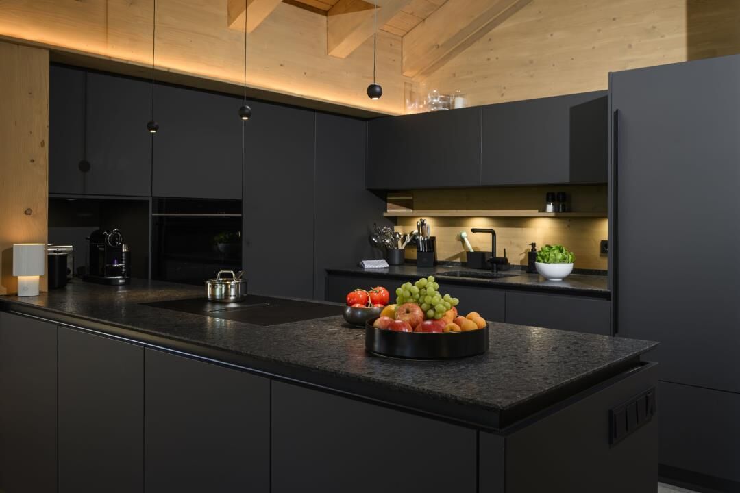 Een moderne keuken met donkere kastjes, een granieten aanrechtblad en een fruitschaal.