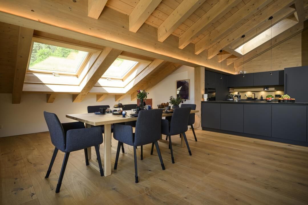 Een moderne keuken met dakramen, een eethoek met een tafel en stoelen, en uitzicht op groen.
