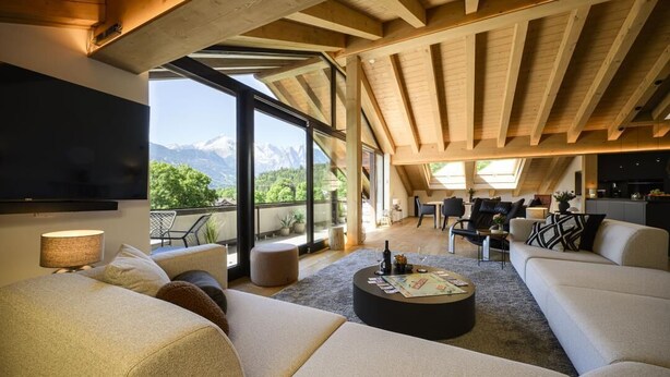 A spacious living area with a large sofa, a coffee table, and a TV mounted on the wall. - Alpine Loft Marianne über Garmisch-Partenkirchen (Garmisch-Partenkirchen)