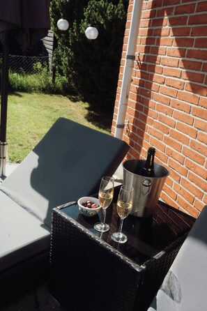 Eine Terrasse mit Tisch, zwei Liegestühlen, einem Champagnerkühlbag und einer Flasche.