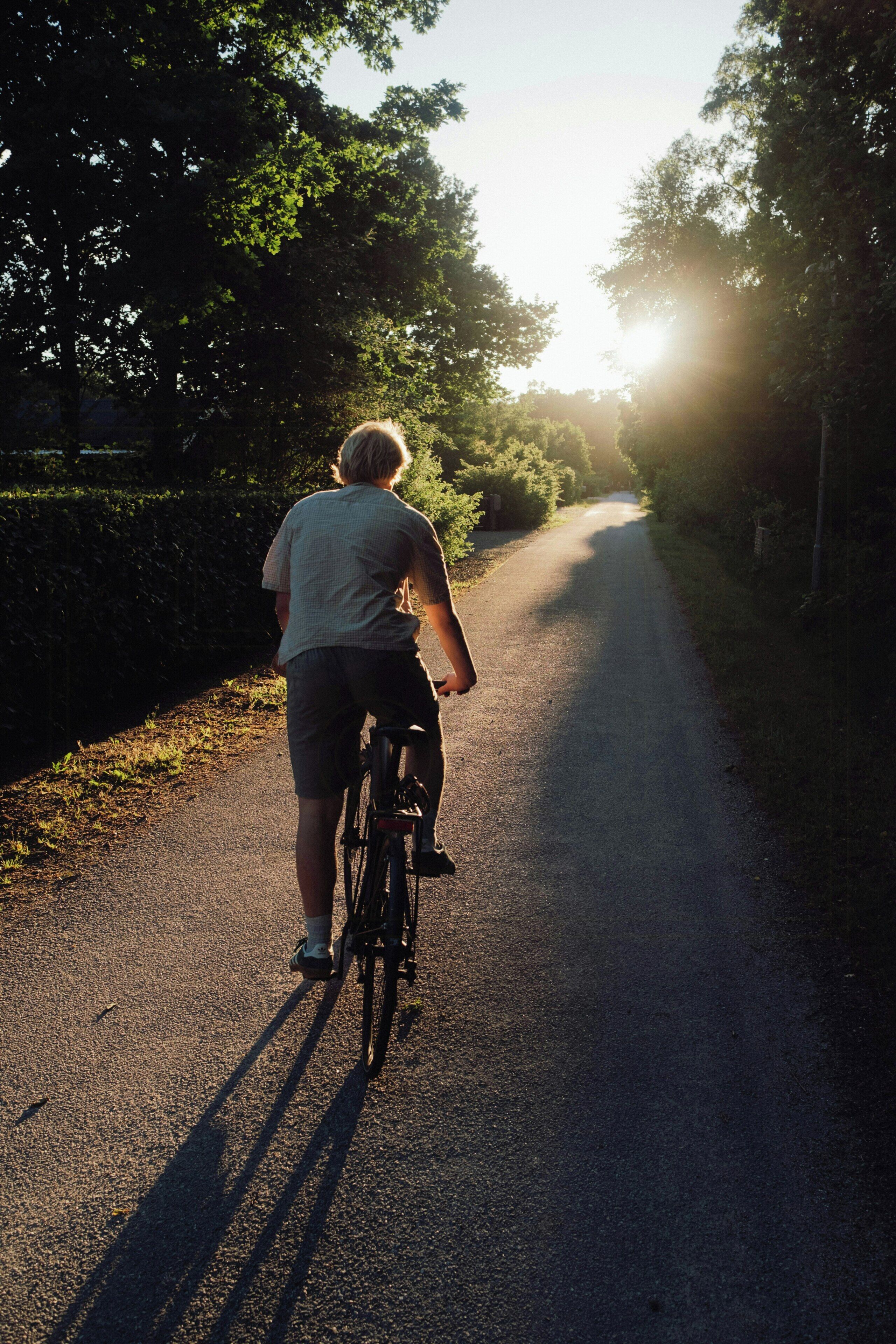 A person riding a bicycle on a paved path surrounded by trees.