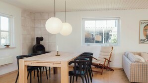 Uma área de jantar moderna com mesa de madeira, cadeiras pretas e luminária pendente branca.