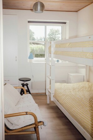 Een slaapkamer met een stapelbed, bureau, stoel en een raam.