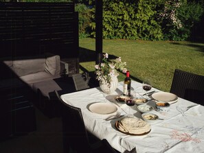 Een terras met een eettafel gedekt voor twee personen, een fles wijn en een bloevas.