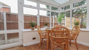 A conservatory with a glass roof, wicker furniture, and potted plants. - 31 Llys Ogwen (Prestatyn)