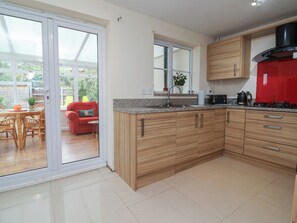 A modern kitchen with wooden cabinets, a red appliance, and a sliding glass door leading to a patio area. - 31 Llys Ogwen (Prestatyn)