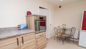 A compact kitchen with wooden cabinets, a stainless steel oven, and a small dining table with chairs. - 31 Llys Ogwen (Prestatyn)