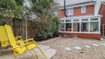 A patio with yellow chairs, a wooden fence, and a brick house with a window.