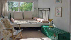 A bedroom with a bed, a green trunk, a rocking chair, and a window with a view of trees. - Cottage in woodland garden in natural harmony (Asnæs)