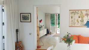 A room with a white table, a guitar, a framed picture, and a botanical illustration on the wall. - Cottage in woodland garden in natural harmony (Asnæs)