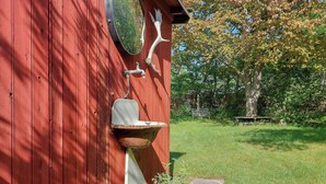 A red wooden structure with a rustic outdoor sink, a metal spout, and a decorative horn. - Cottage in woodland garden in natural harmony (Asnæs)