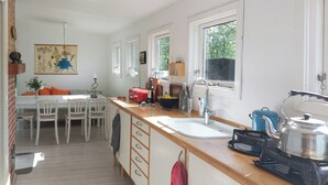 A kitchen with a wooden countertop, a sink, a kettle, and a dining area with chairs and a table. - Cottage in woodland garden in natural harmony (Asnæs)