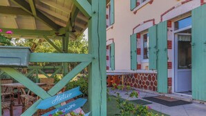 A building with green shutters, a covered outdoor seating area, and a sign indicating 'Atelier Principe.' - Traditional house in the heart of Trensacq forest (Trensacq)