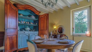 A dining room with a round wooden table set for four, surrounded by chairs. A large wooden cabinet with shelves is to the left, and a window with a view of trees is to the right. - Traditional house in the heart of Trensacq forest (Trensacq)