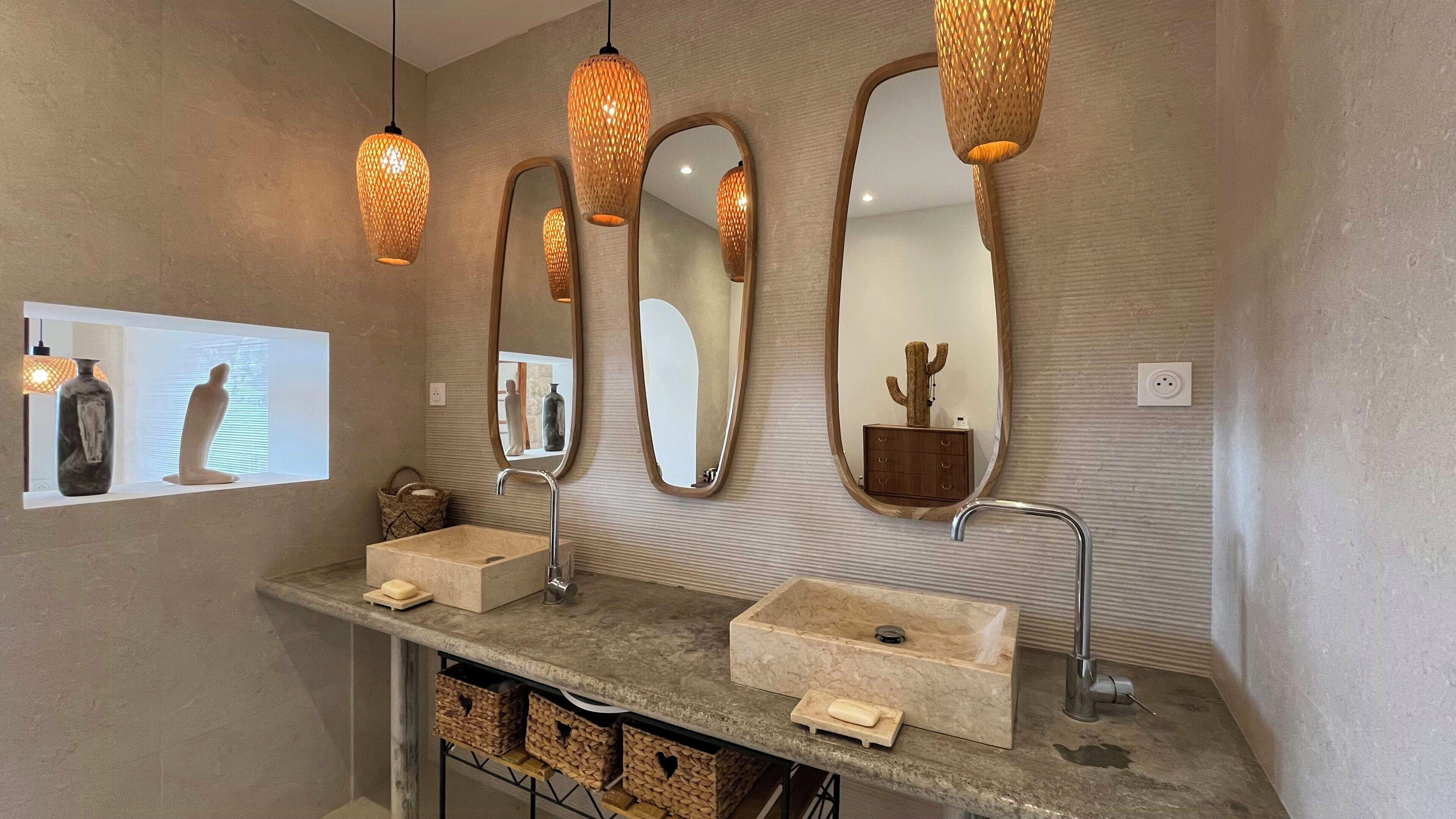 A bathroom with a double sink, three mirrors, and hanging pendant lights.