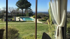 Una piscina con un pérgola, un árbol grande y vistas a montañas distantes.