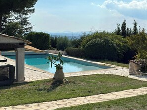 A swimming pool with a stone deck, surrounded by greenery and a view of distant mountains. - Provencal villa with pool and panoramic views (La Gaude)