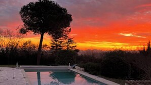 Una piscina con un árbol en primer plano y una puesta de sol al fondo.
