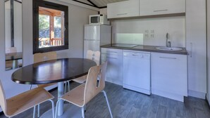 A compact kitchen with white cabinets, a microwave, a dishwasher, and a dining area with a round table and chairs. - Quiet Detached Chalet for Five (Sollies-Toucas)